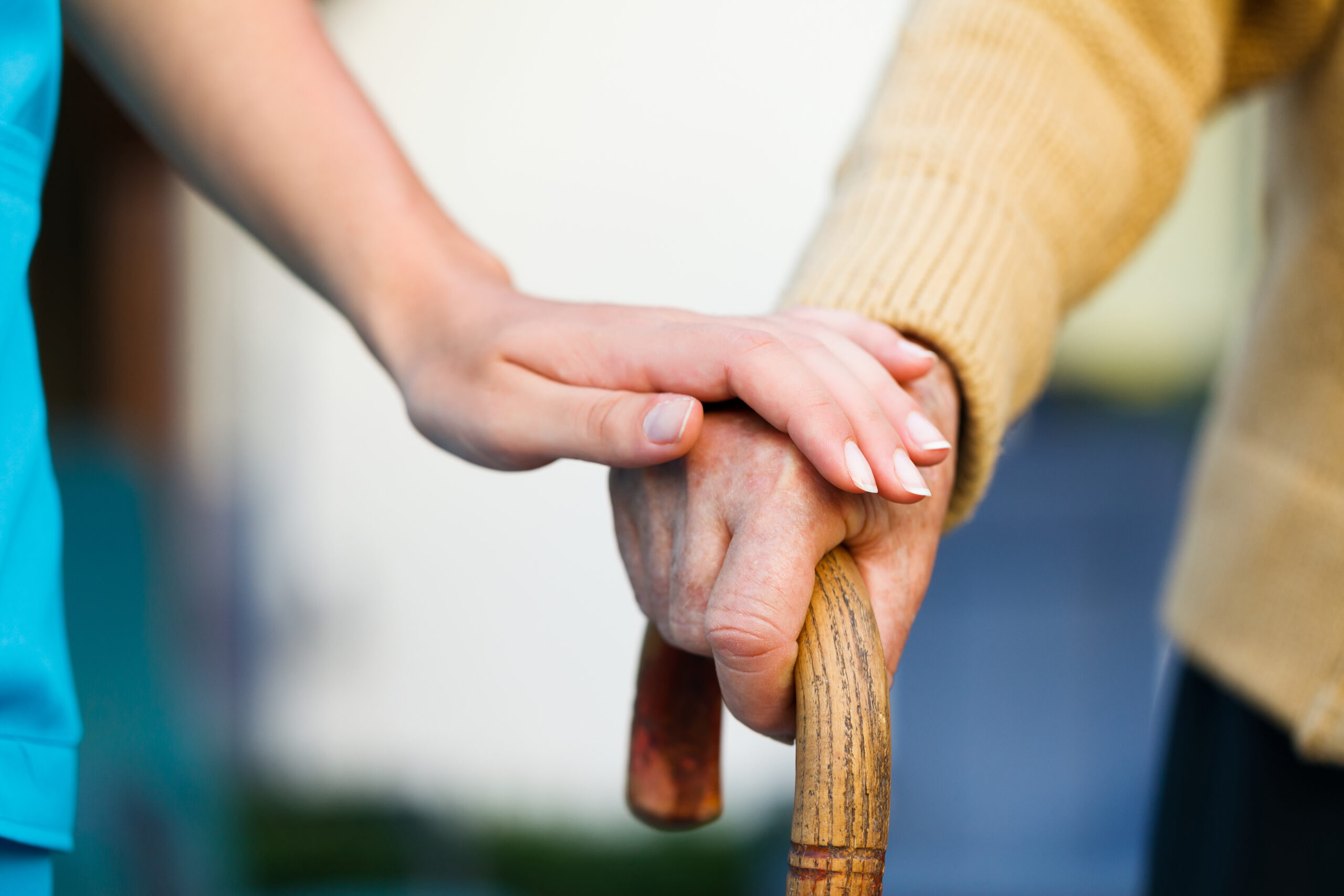Young caregiver holding an elderly person's hand on a cane for support and stability.