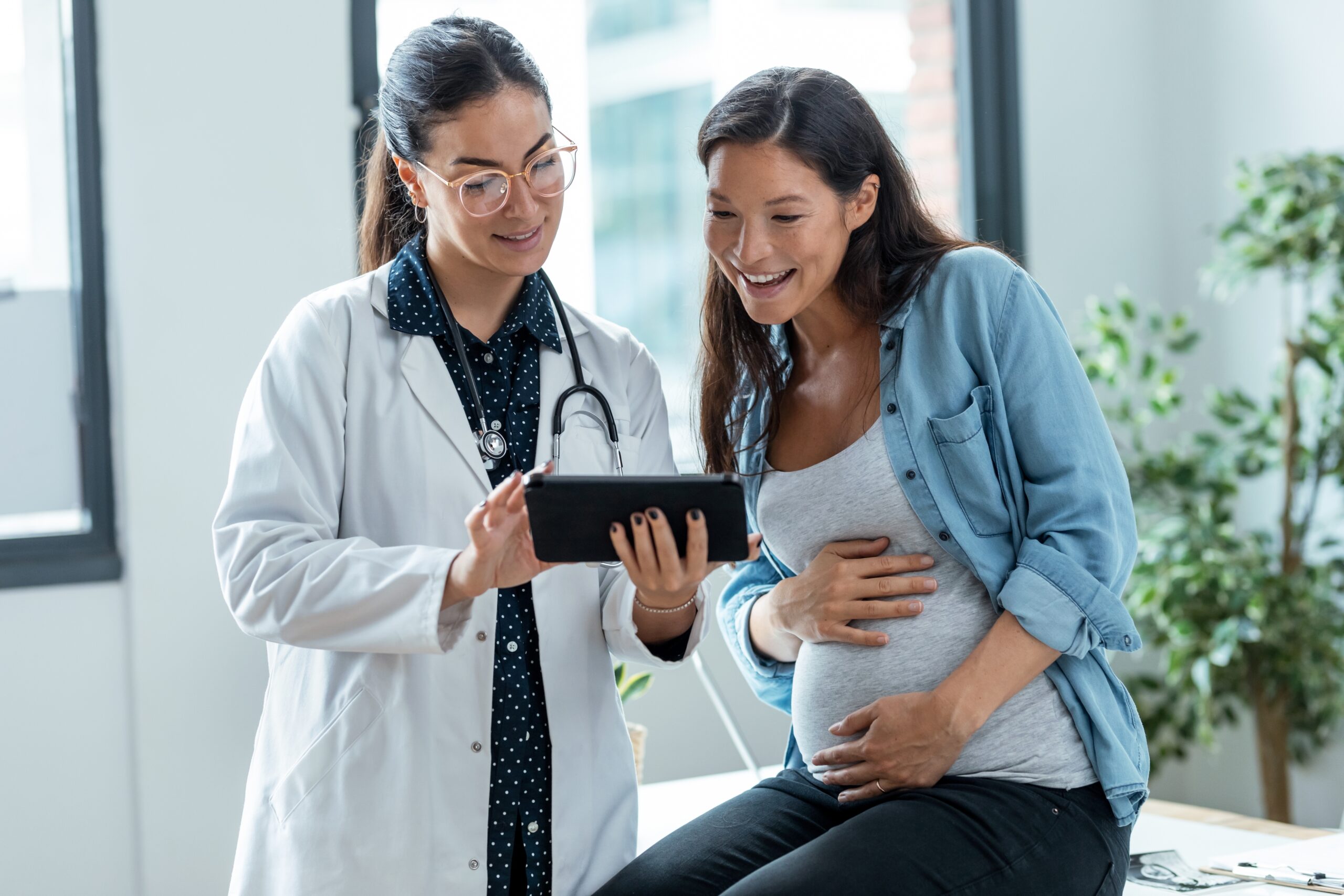 Doctor consulting with a pregnant woman about medical equipment options on a digital tablet.