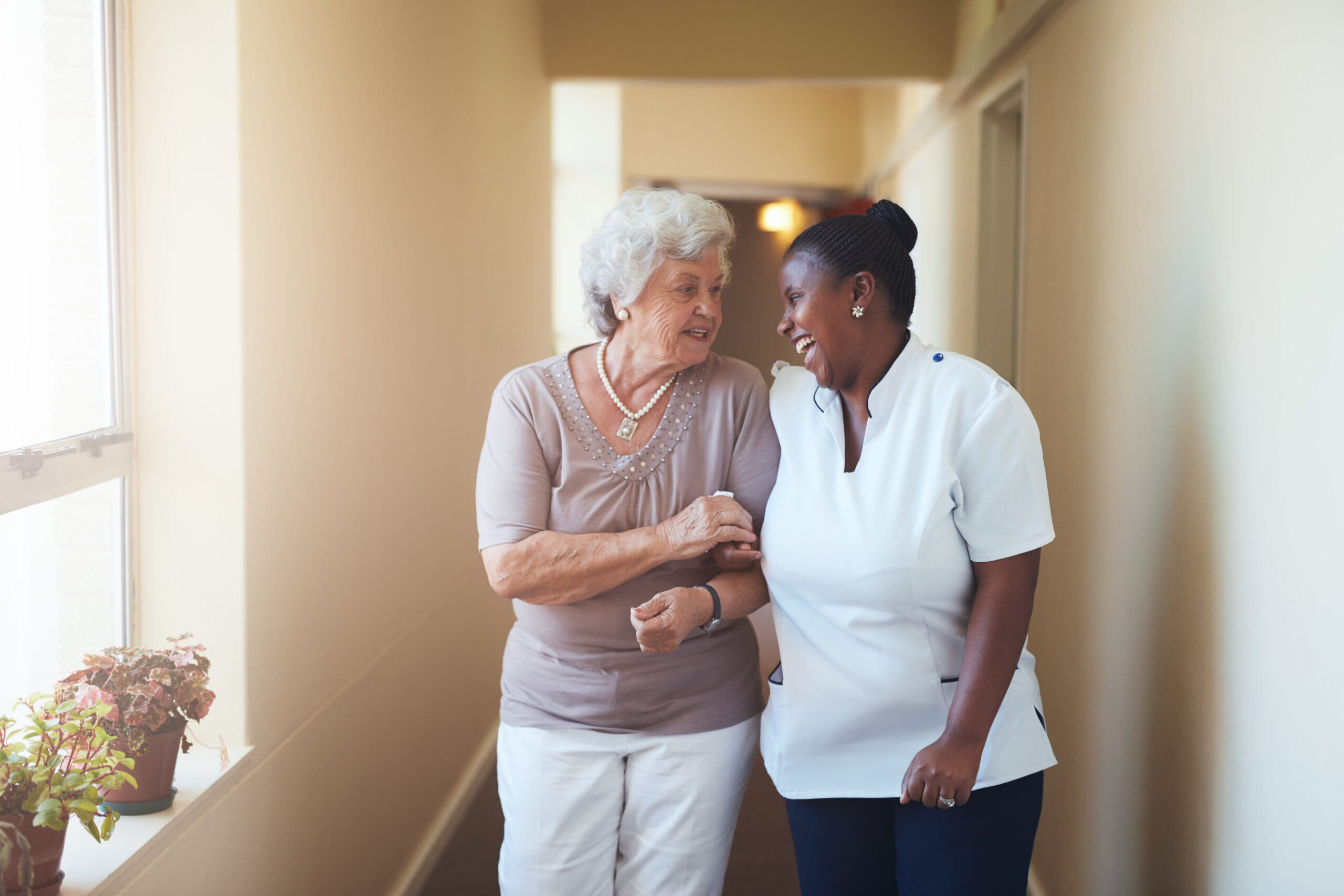 Elderly woman being guided by a healthcare professional through a hallway, symbolizing assistance with Medicare.