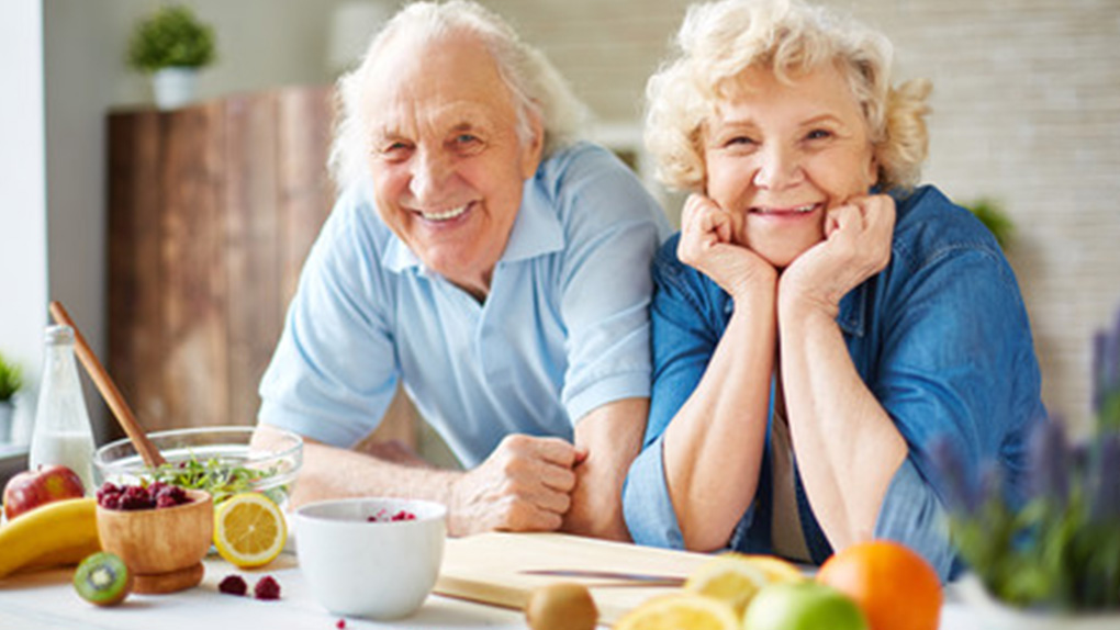 Older couple smiling at the dinner table with fruit and salad