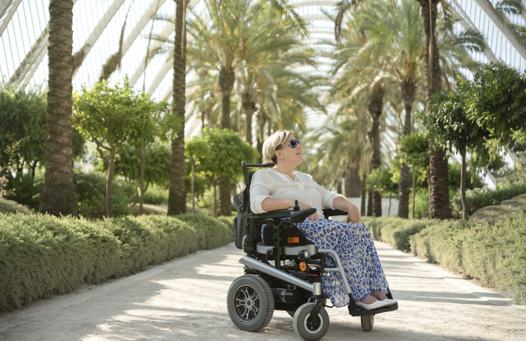 a smiling woman sitting in the electric wheelchair with disability in the garden of the city park